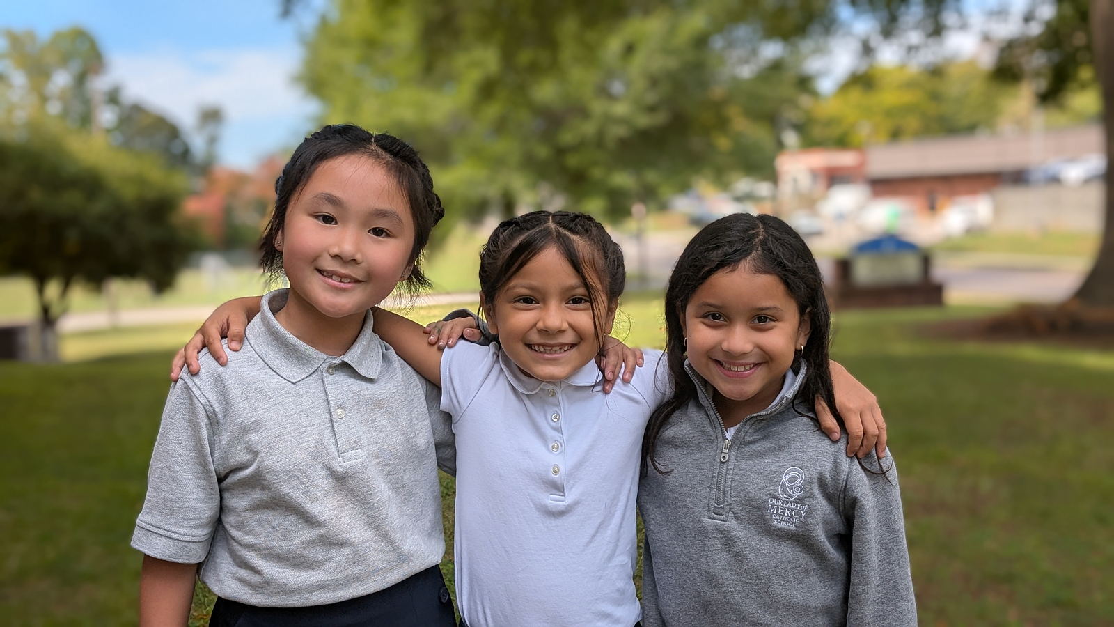 three girls hugging, smiling and looking at the front with their school uniforms 
