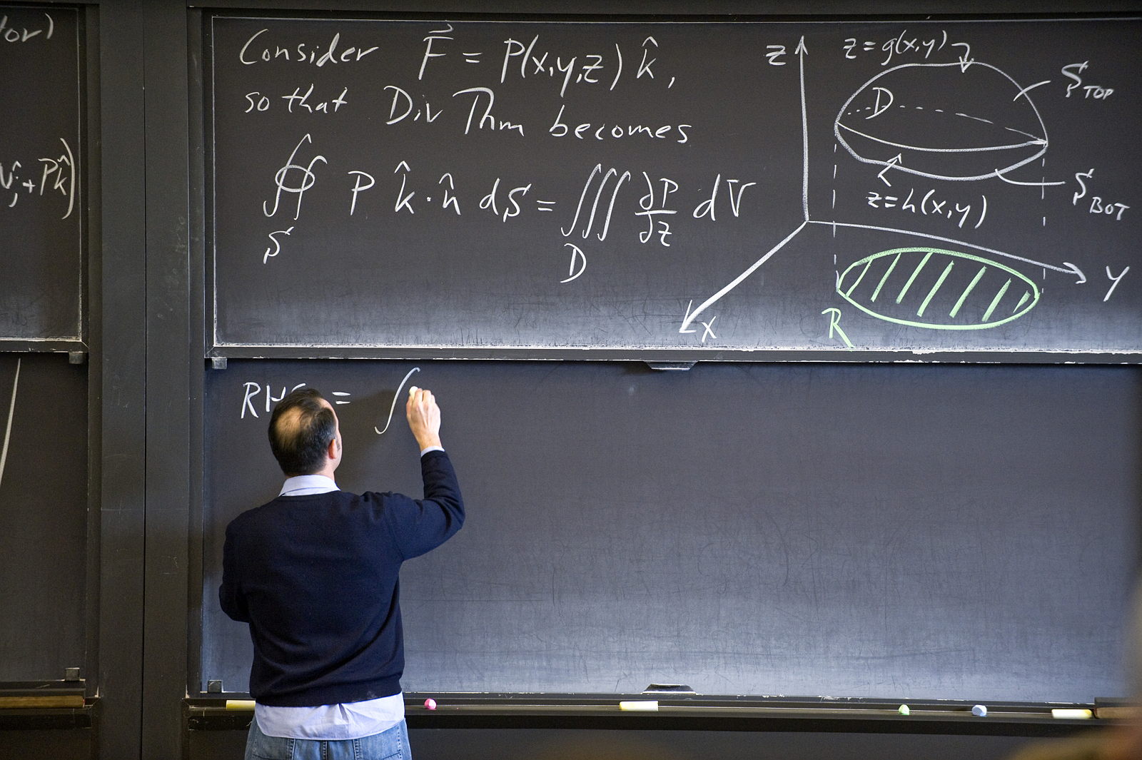 A man writes on a chalkboard full of equations