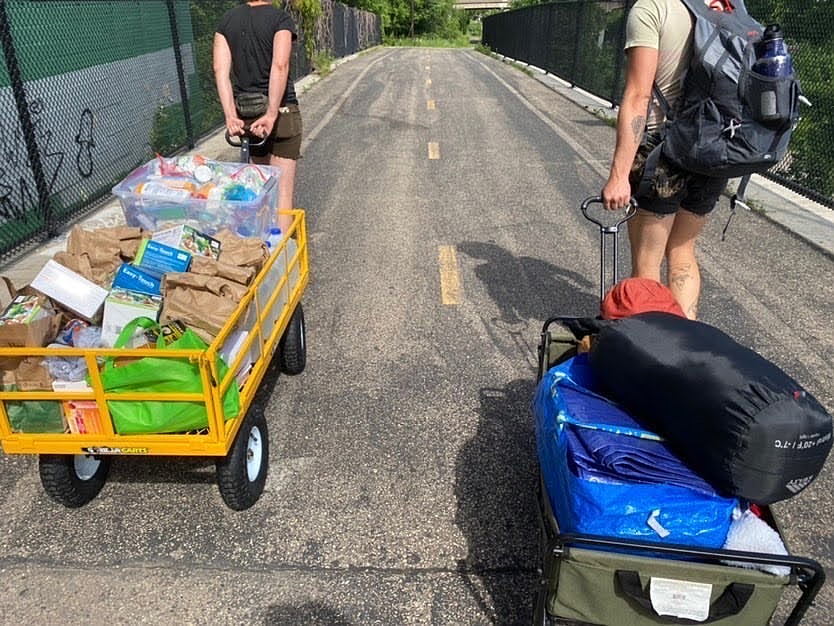 Photo of two people pulling wagons filled with harm reduction supplies, tents, and sleeping bags on the Greenway bike path