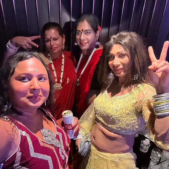 A group of four South Asian Trans Women put up peace signs and smile at the camera. 