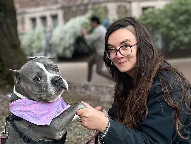 Girl holds dog's paw as they both look at the camera