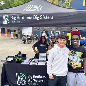 Big Brother Isaac and Little Brother Ethan pose in front of the Big Brothers Big Sisters Twin Cities table at the CLUES 2024 Latino Festival