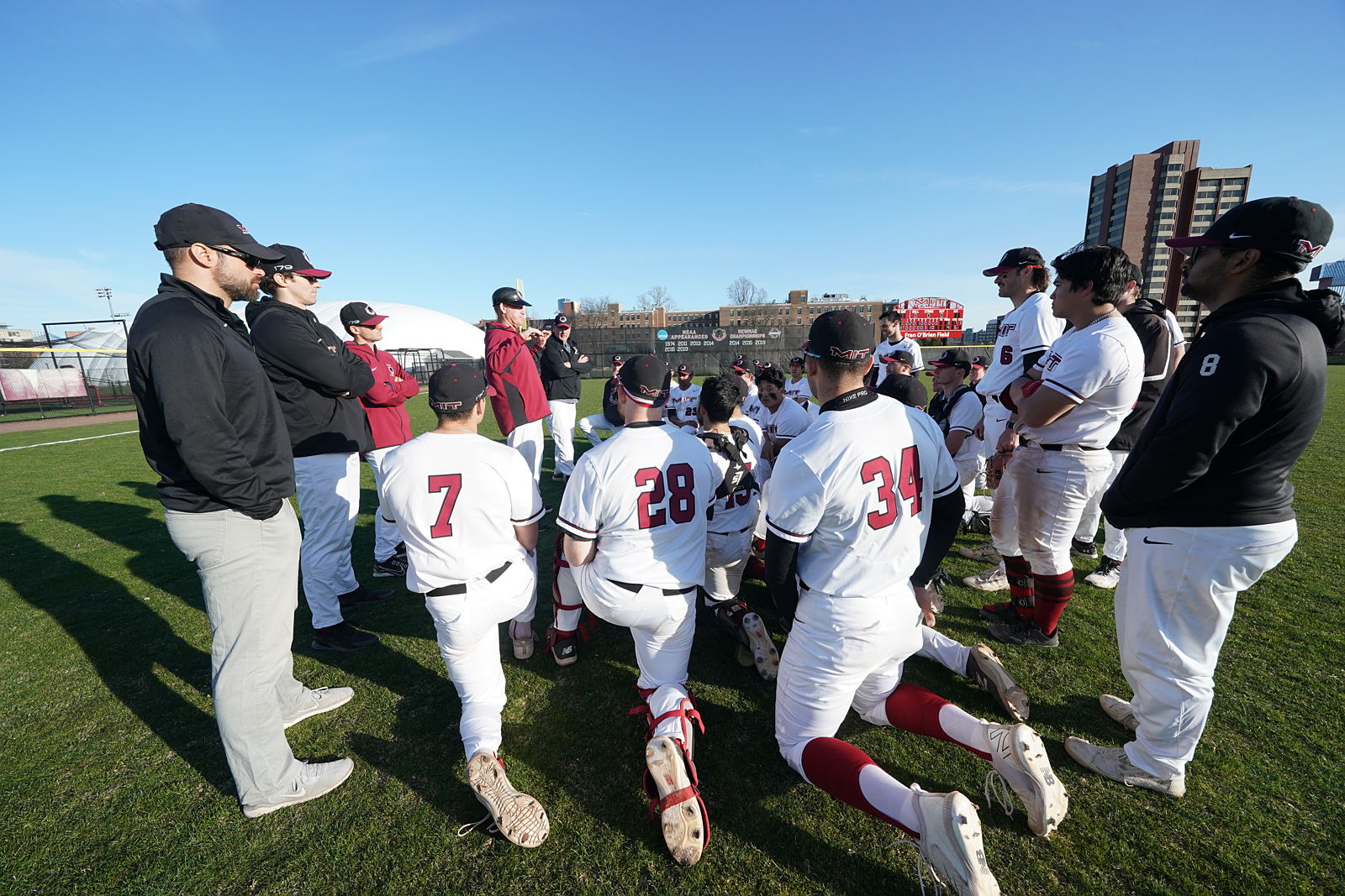 The MIT baseball team kneel on the field.
