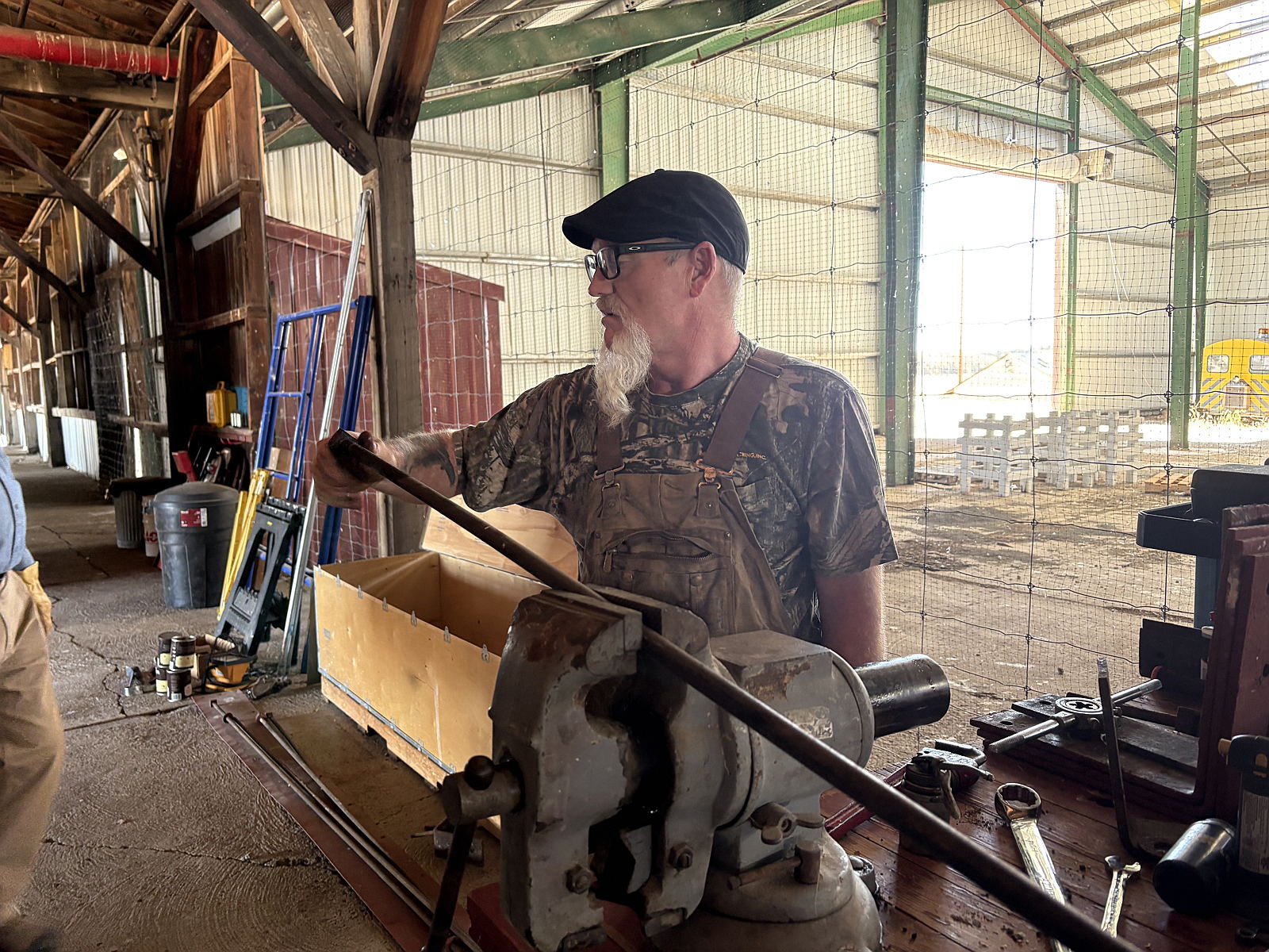 A volunteer works on repairing threads for a support rod secured in a bench vise beside Boxcar No. 518.