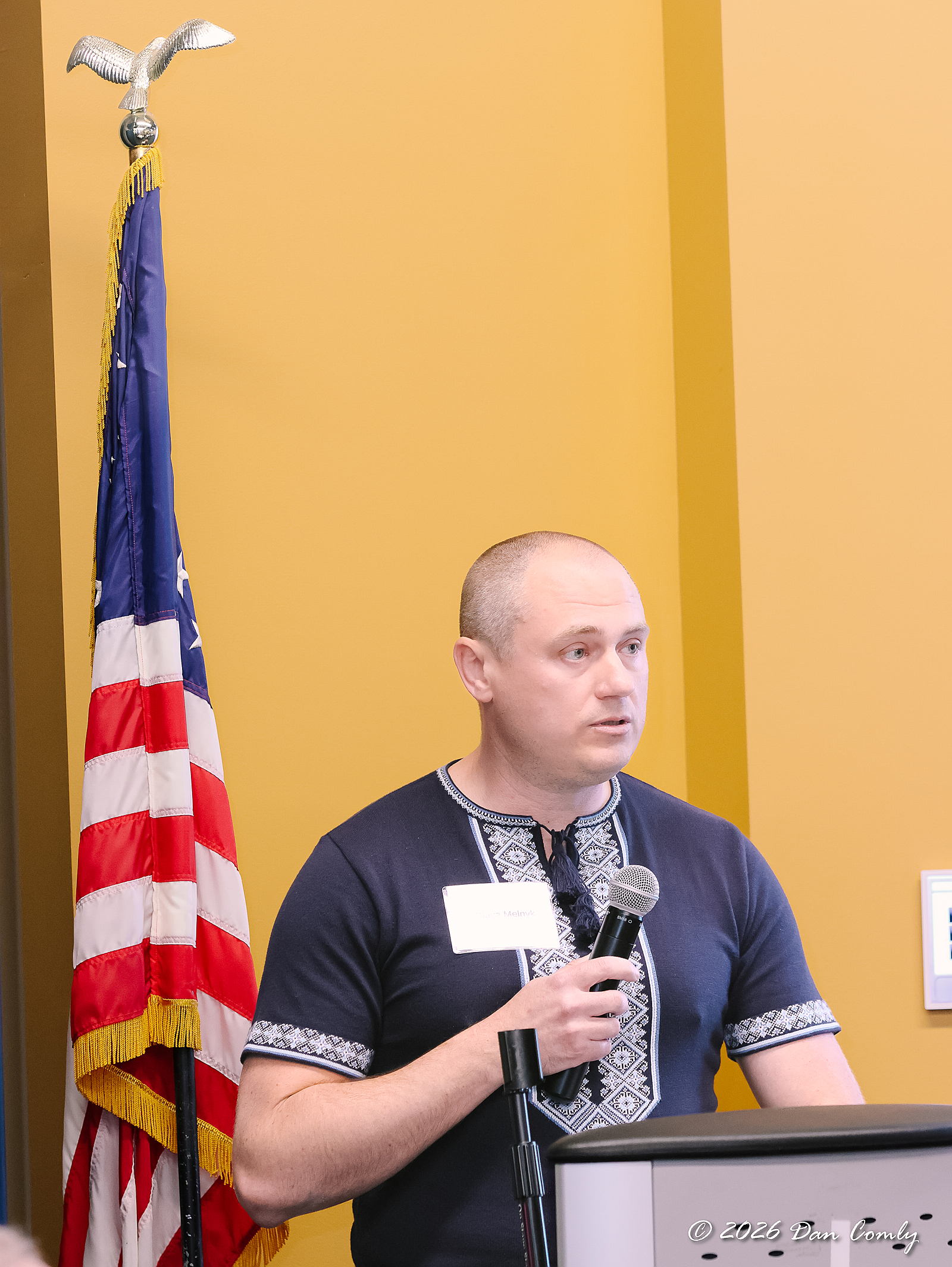 A man in traditional Ukrainian clothing speaks at a podium in front of the American Flag.