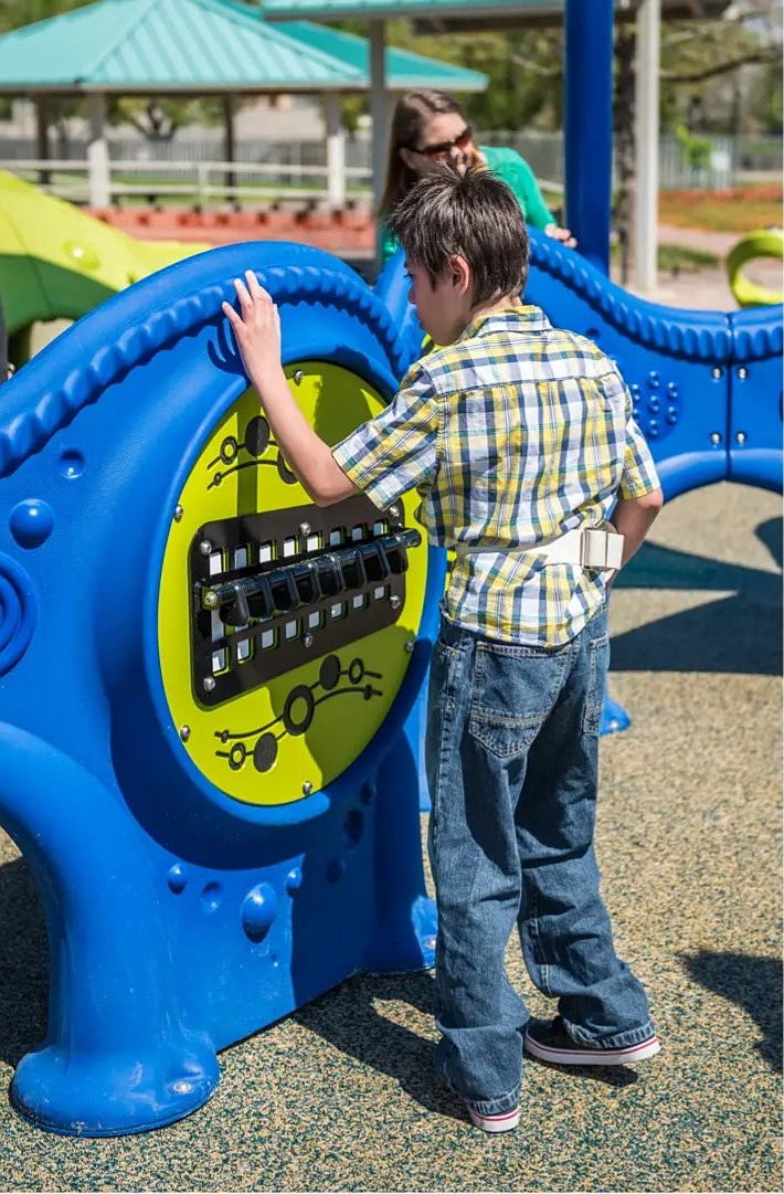 Child wearing back brace touches texture of interactive musical playground feature