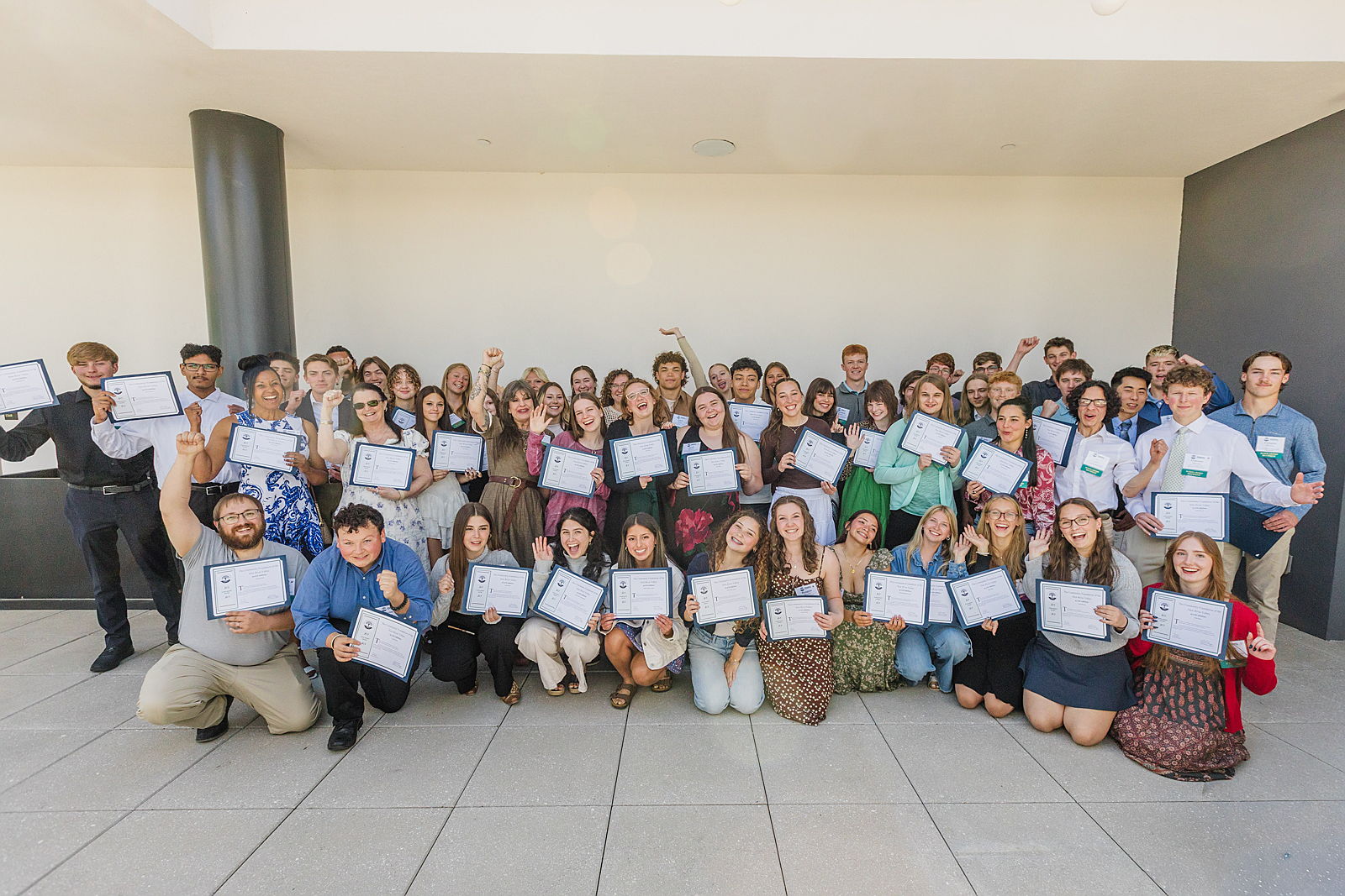 Several dozen scholarship students hold certificates and celebrate