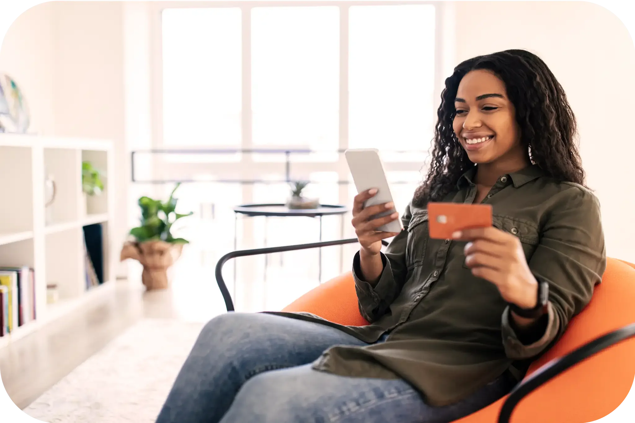 oyful woman sitting in a chair with a tablet in one hand and a gift card in another.