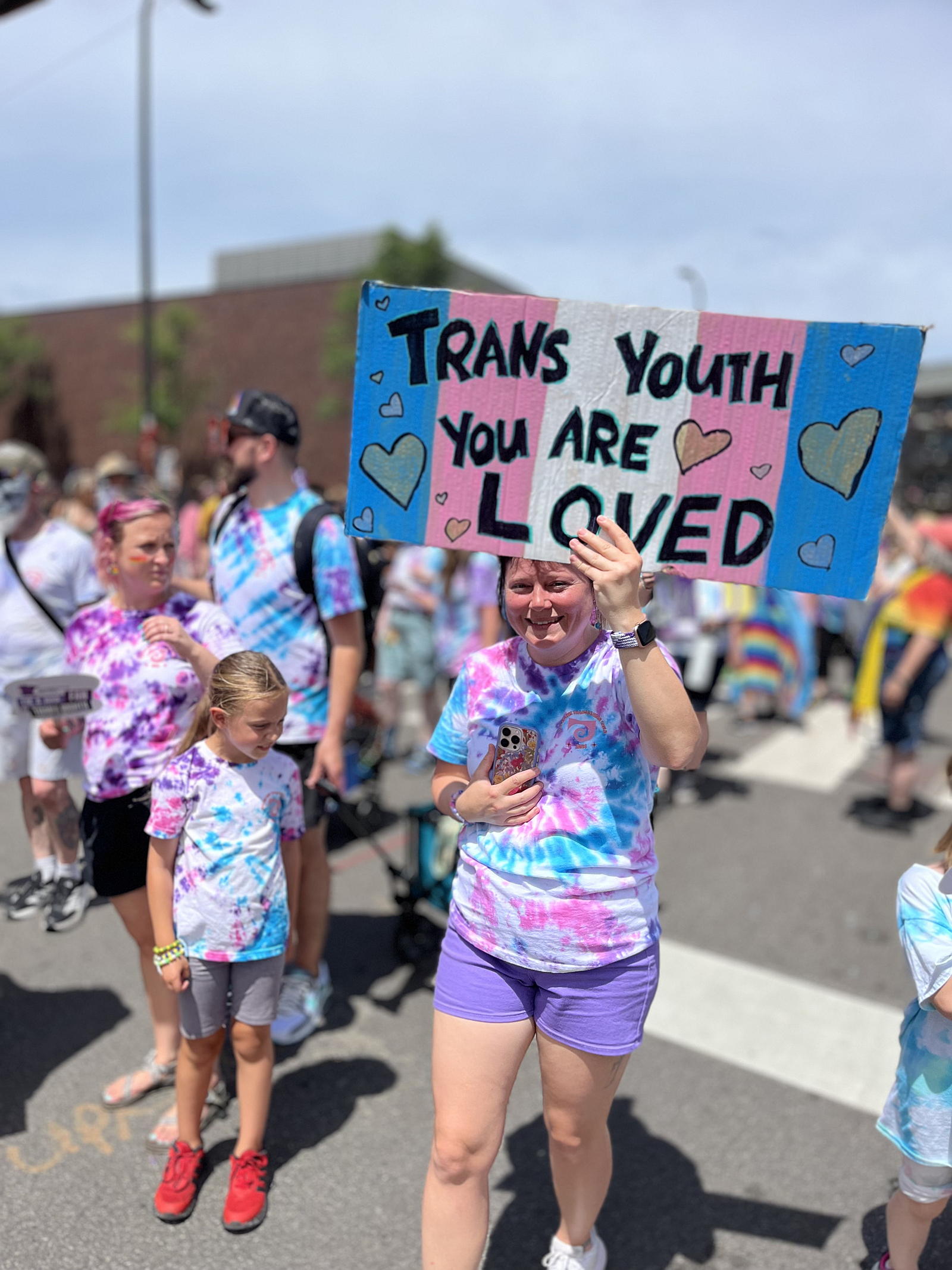 A person marching, holding as a sign that says "Trans Youth Are Loved."
