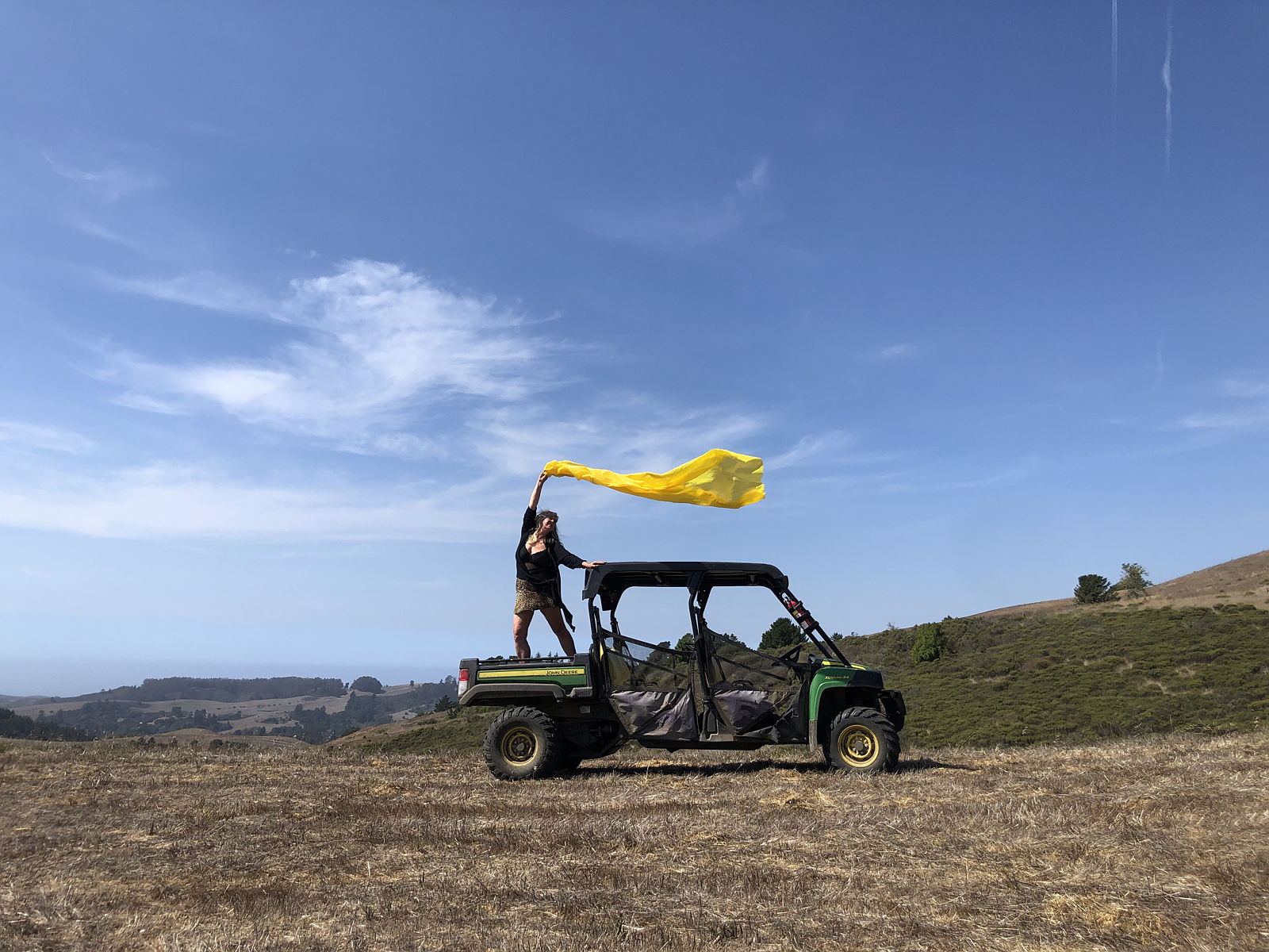 April Sellers waving a large yellow flag on the bed of a Gator off road vehicle in the Mountains of Woodside, CA