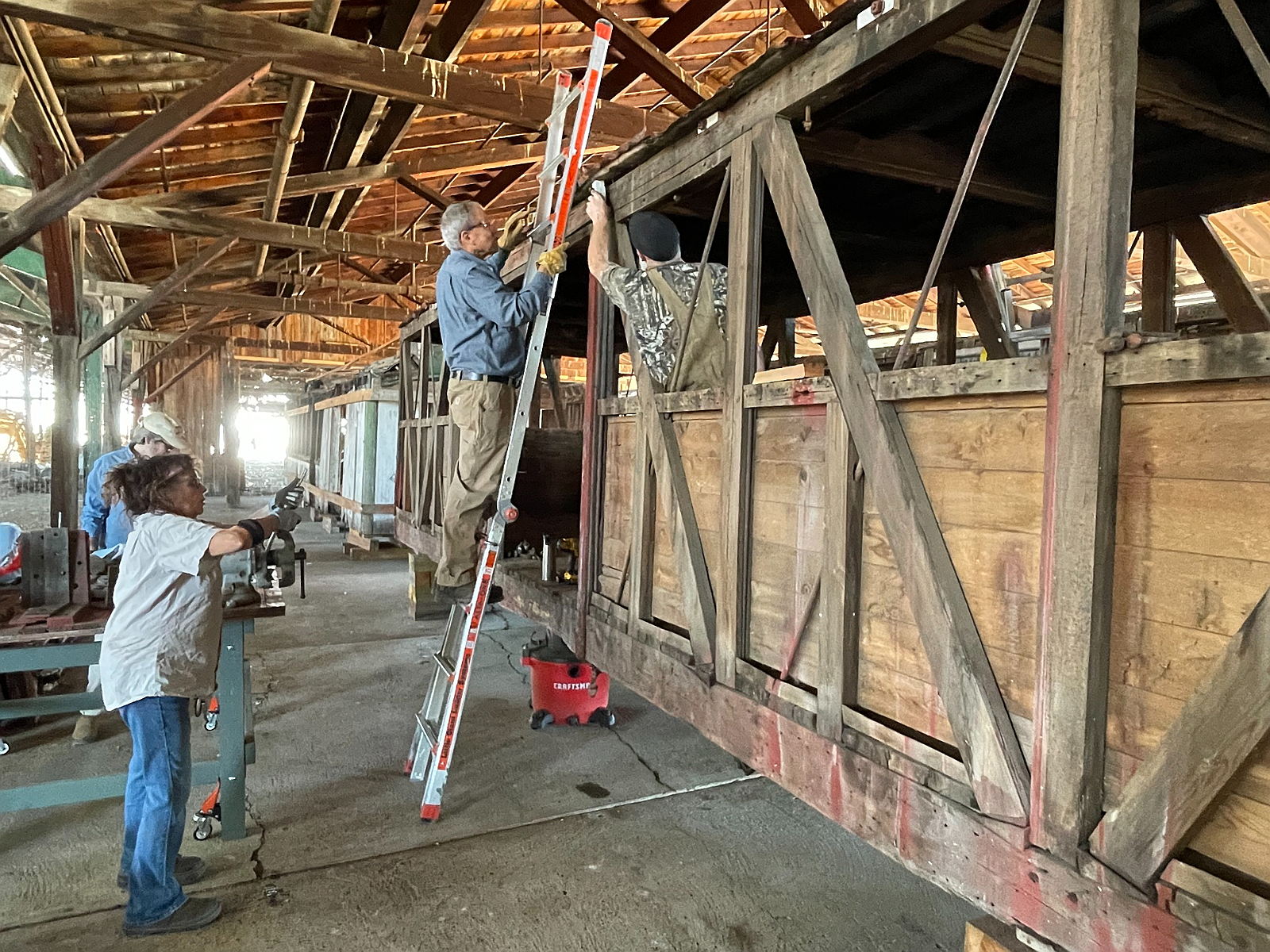 Volunteers work along the exposed wooden frame of N-C-O Railway Boxcar No. 518 inside the car barn in Alturas.