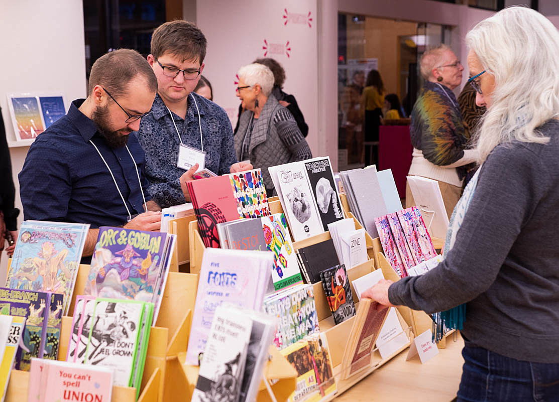 Multiple guests browse through a zine display set up in the gallery.
