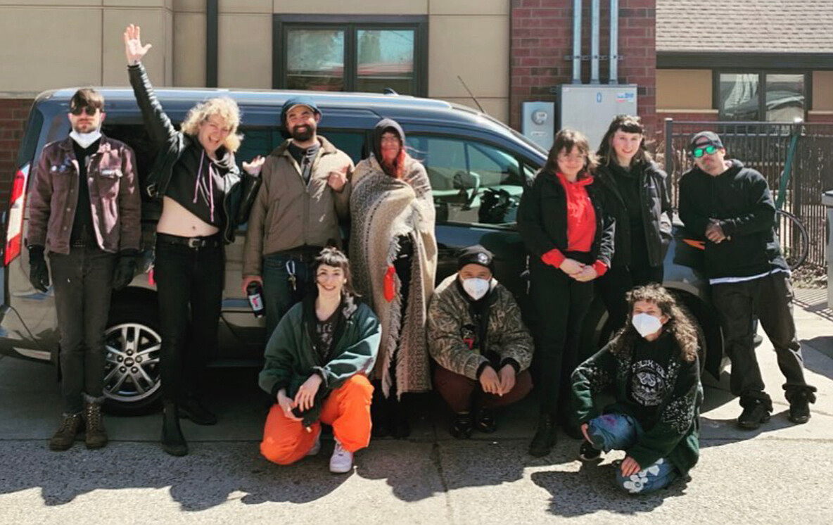 Photo of a group of Southside staff standing and kneeling with happy and excited expressions in front of a grey delivery van parked outside the Southside office