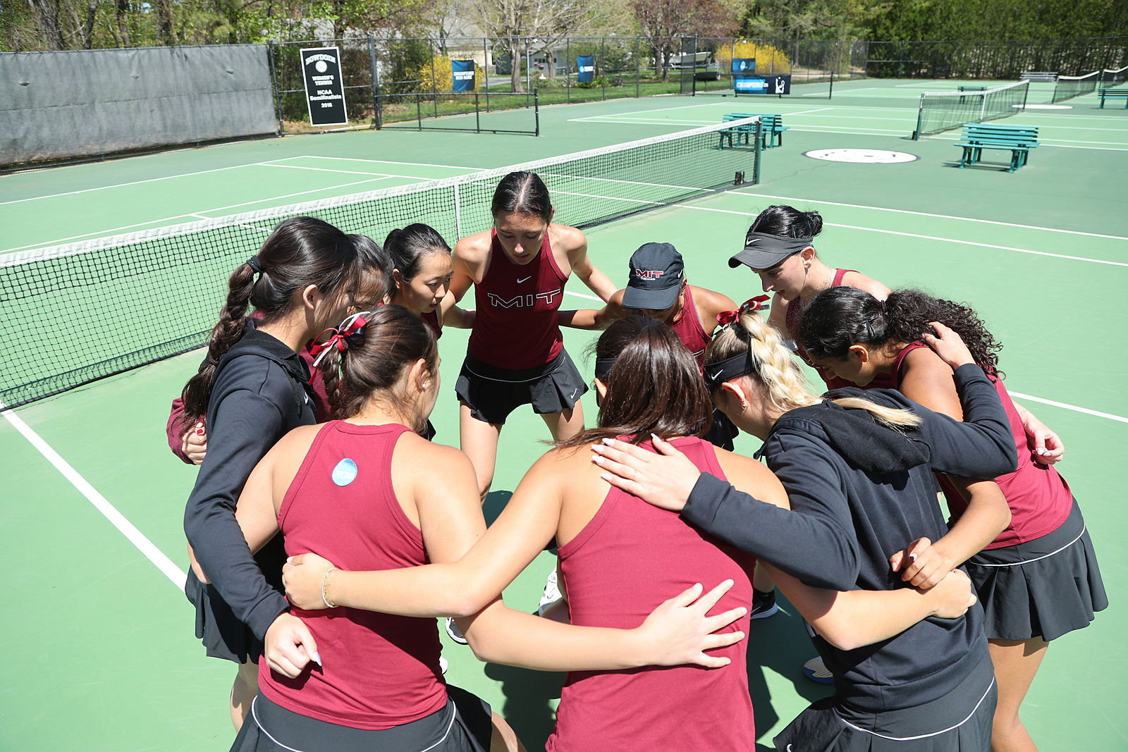 Women's tennis team members huddle on the court